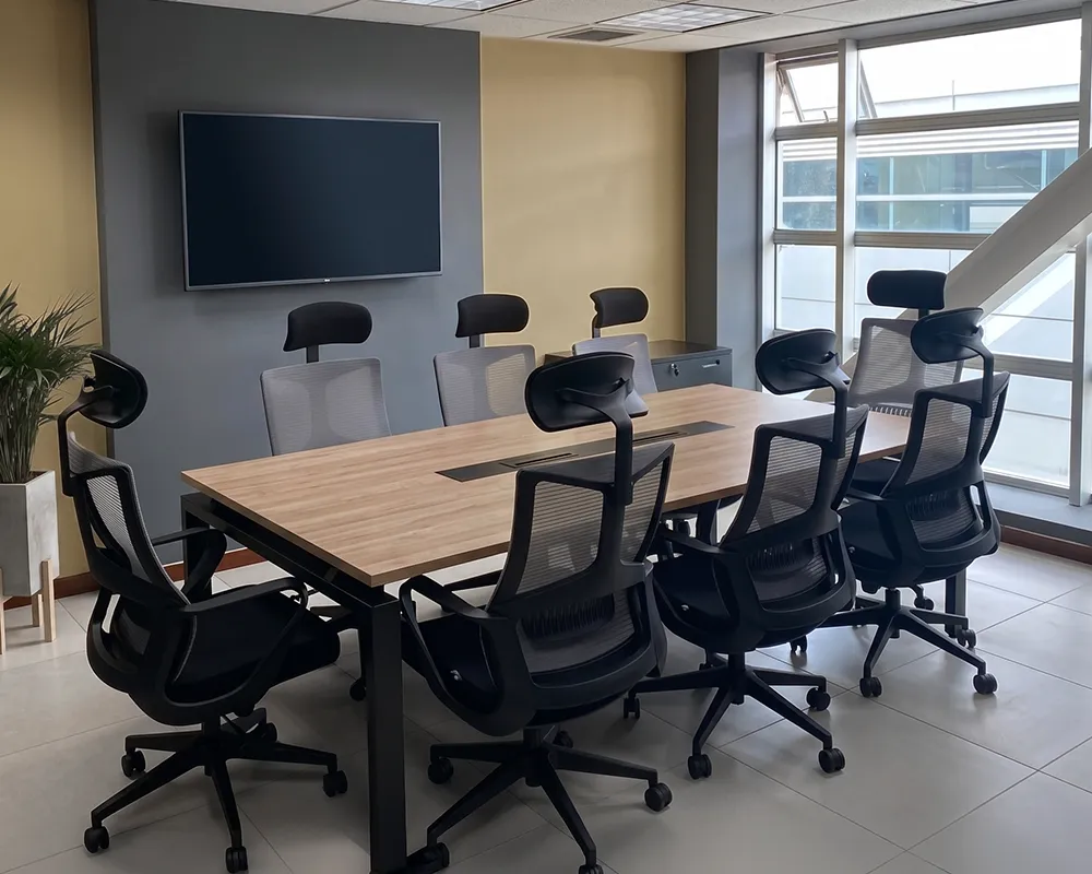 Mesa para oficina tipo junta en madera natural con sillas ergonómicas negras en una sala de reuniones corporativas